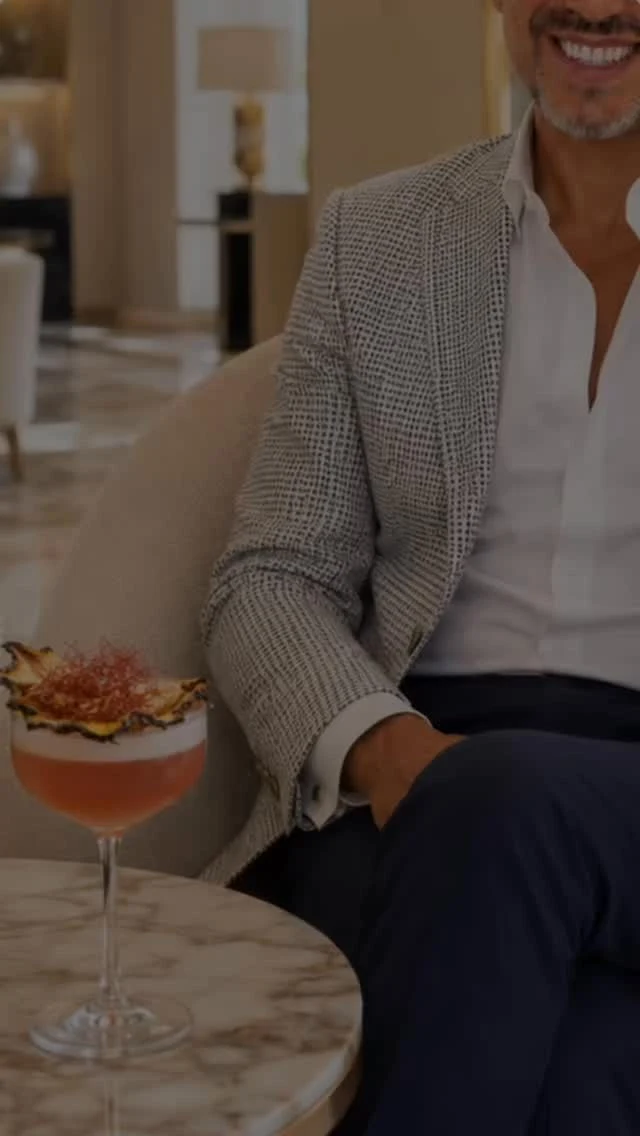 Americana de punto gris y camisa blanca, junto a un cóctel sobre una mesa de mármol
