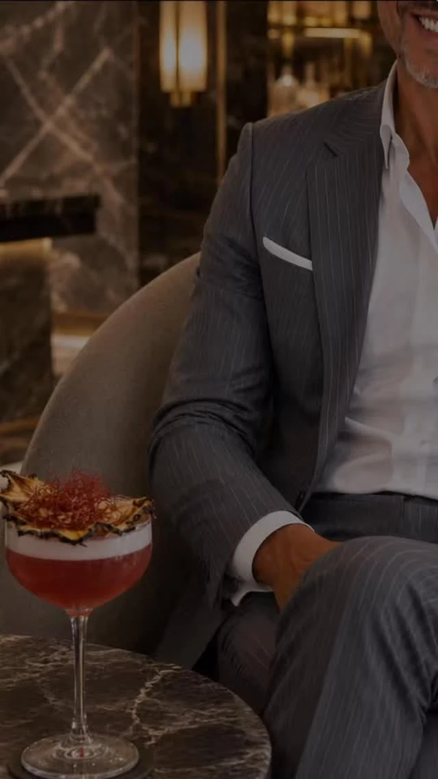 Traje gris de raya diplomática y camisa blanca, junto a un cóctel sobre una mesa de mármol
