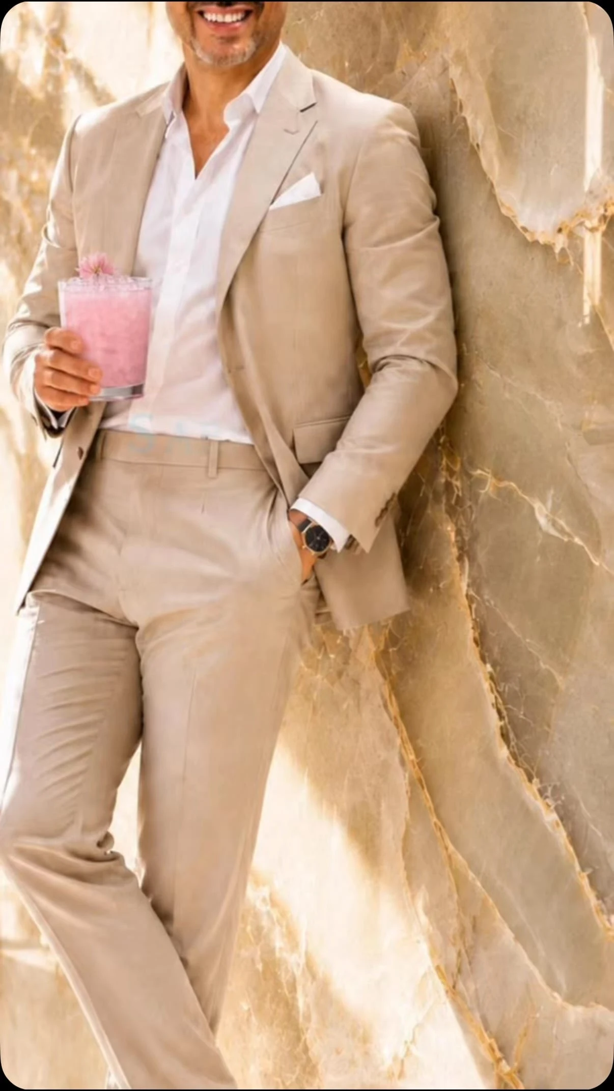 Traje beige y camisa blanca, con un cóctel rosa en la mano